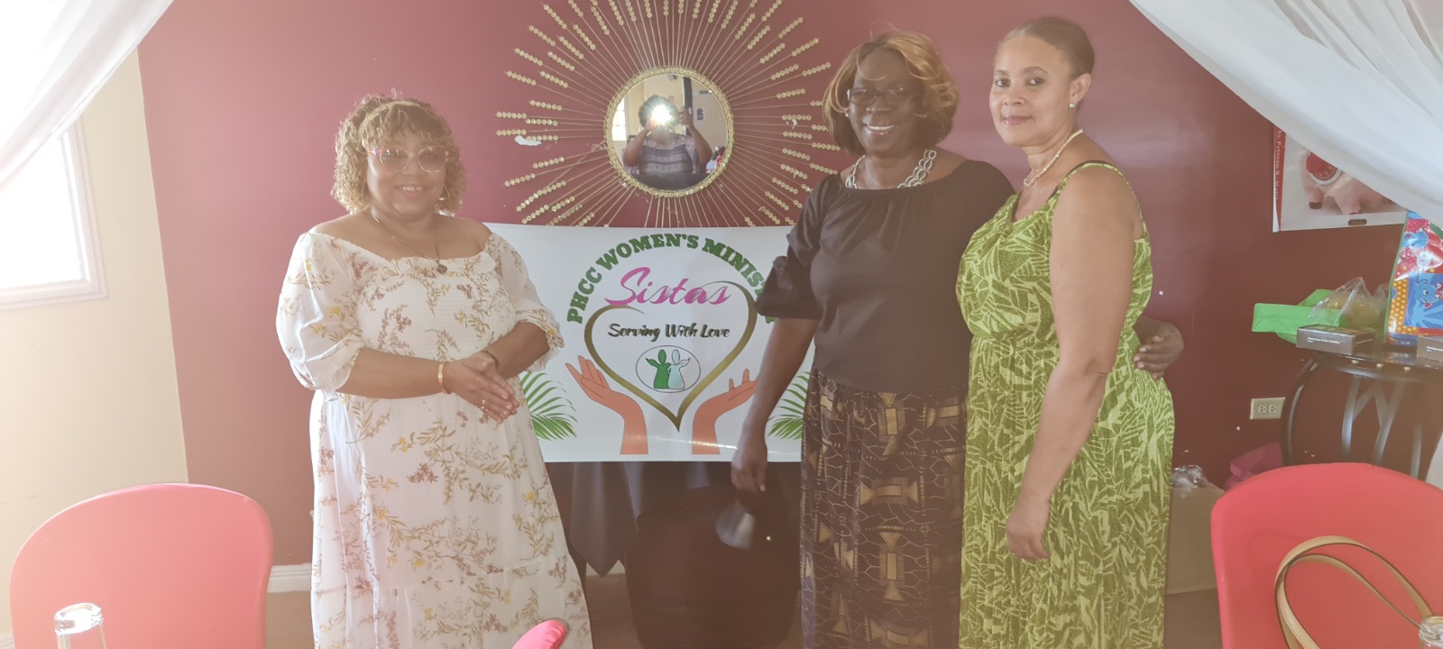 Three women standing with the PHCC Women's Ministry Sistas banner
